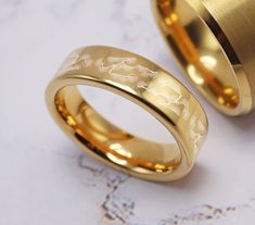 two gold wedding rings sitting next to each other on a marble surface with white background