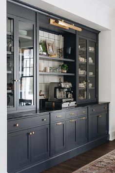 a black and gold china cabinet in a white walled dining room with wood floors, glass doors, and rug on the floor