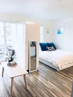 a room with a bed, desk and mirror in it on the floor next to a window