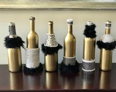 several wine bottles are decorated with black feathers and bling on the top one is gold