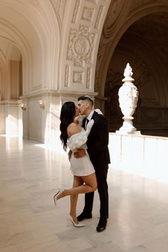 a man and woman are kissing in an ornate room with white marble flooring, arched archways and columns