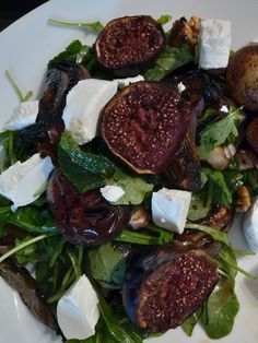 a salad with figs, cheese and spinach leaves on a white platter