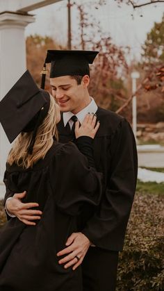 a man and woman in graduation gowns hugging each other while they are standing outside