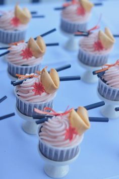 small cupcakes with pink frosting and sprinkles on sticks are arranged in rows