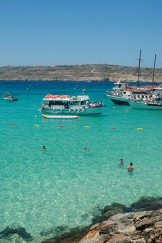 several boats are in the water near some rocks and people floating on them at the beach