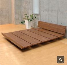 a wooden bed frame sitting on top of a hard wood floor next to a potted plant