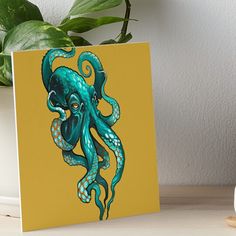 an octopus art board print on a table next to a potted plant and white vase