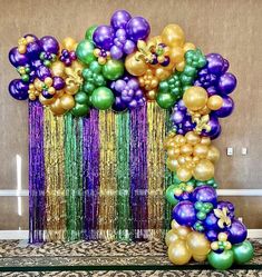 the balloon arch is decorated with gold, purple, and green balloons that are attached to streamers