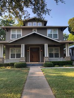 a brown house with white trim on the front porch and two large trees in front of it