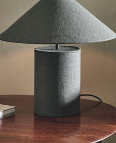 a table lamp on top of a wooden table next to a book and remote control