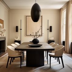 a dining room table with white chairs and a black vase on the center, in front of a fireplace