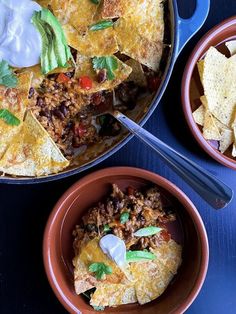 two bowls filled with mexican food next to some tortilla chips and sour cream