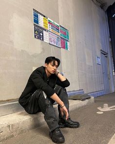 a young man sitting on the ground next to a wall