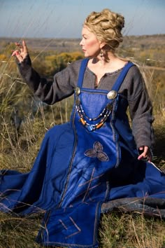 a woman sitting on the ground in a blue dress and holding her hand out to something