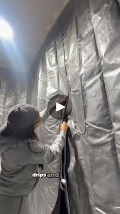 a woman in grey jacket and hoodie holding up a mirror with light shining on it