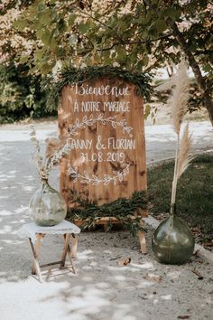 a wooden sign sitting next to two vases on top of a cement floor under a tree