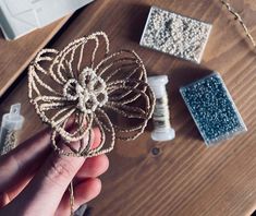 a hand holding a piece of string art on top of a wooden table next to sewing supplies