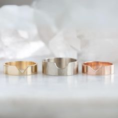 three gold and silver rings sitting on top of a white table next to each other