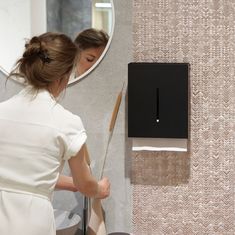 a woman standing in front of a mirror holding a large pair of scissors next to a wall mounted paper towel dispenser