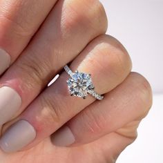 a woman's hand holding a diamond ring on top of her finger, with the middle