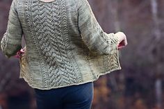 a woman wearing a green sweater and blue pants is walking through the woods with her hands in her pockets