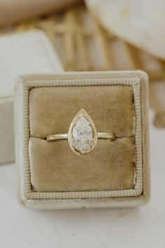 an engagement ring with a pear shaped diamond sits in a box on top of a table