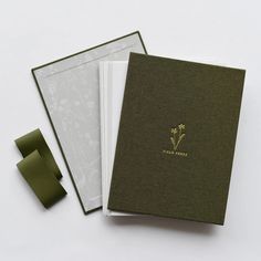 two notebooks sitting next to each other on top of a white table with green ribbon