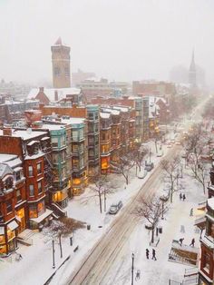 a city street covered in snow and surrounded by tall buildings with clock tower on top