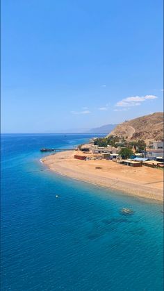 an aerial view of a beach with houses on the shore and blue water in the foreground