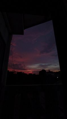 the sun is setting over some trees and hills in the distance as seen from a window