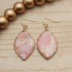 a pair of pink and gold earrings sitting on top of a wooden table next to beads