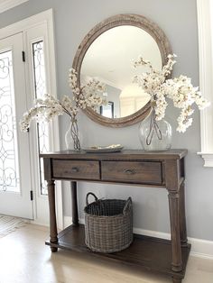 a wooden table topped with a mirror and vase filled with flowers next to a door