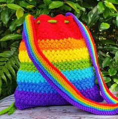 a multicolored crocheted purse sitting on top of a wooden table next to green leaves