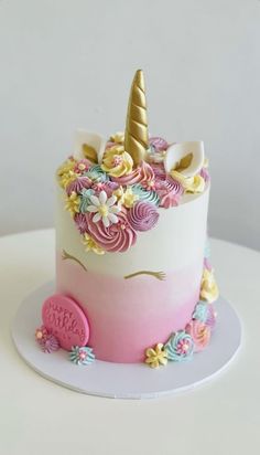 a pink and white cake with a unicorn's face on the top is decorated with multicolored icing