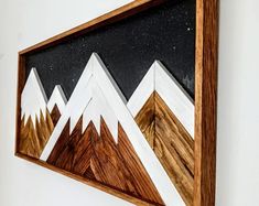 a wooden frame hanging on the wall with mountains and stars painted on it's sides