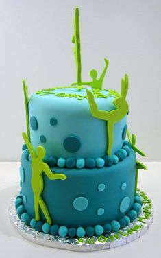 there is a blue cake with green decorations on the top and two people doing acrobatic tricks