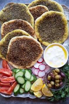 an assortment of food is displayed on a platter, including pita breads and cucumbers