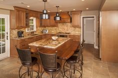 a large kitchen with wooden cabinets and marble counter tops, along with bar stools