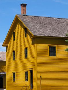 a large yellow house sitting on top of a lush green field next to a forest