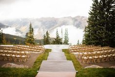 an outdoor ceremony set up with wooden chairs and mountains in the backgrouds