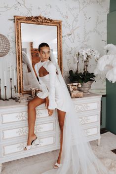 a woman is posing in front of a mirror wearing a white dress and high heels