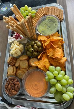 a platter filled with grapes, crackers, nuts and dip