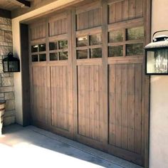 a wooden garage door in front of a brick wall and light fixture on the side