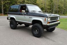 the truck is parked on the side of the road in front of some trees and grass