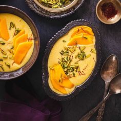 two bowls filled with food on top of a table next to spoons and silverware