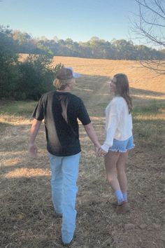 a man and woman holding hands while walking through a field