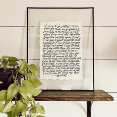 a piece of paper with writing on it sitting next to a potted plant in front of a white wall