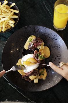 a person is holding a fork over some food on a plate with fries and orange juice