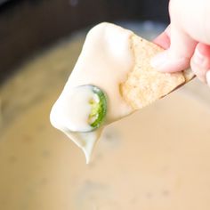 a hand holding a tortilla chip over a pot of soup