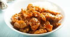 a white bowl filled with meat and rice on top of a blue tablecloth next to a napkin